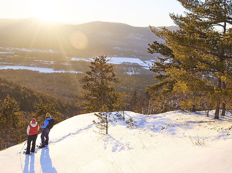 two snowshoers on a cliff admiring the view