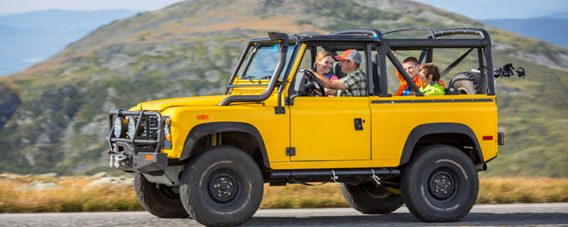 A family riding in a yellow SUV with dramatic mountain view behind them