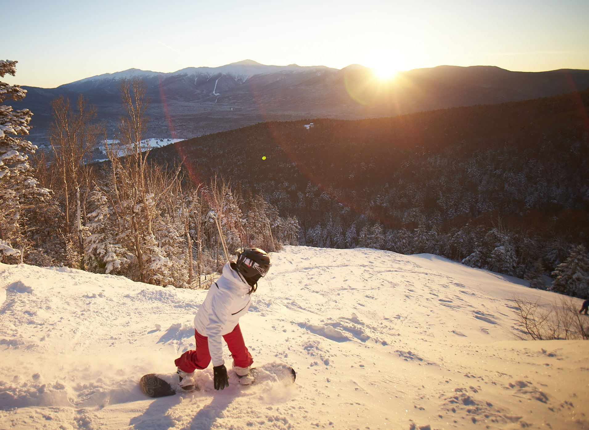 Snowboarder headed down mountain at sunset