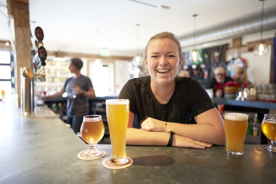 a bartender smiling behind the bar with a beer