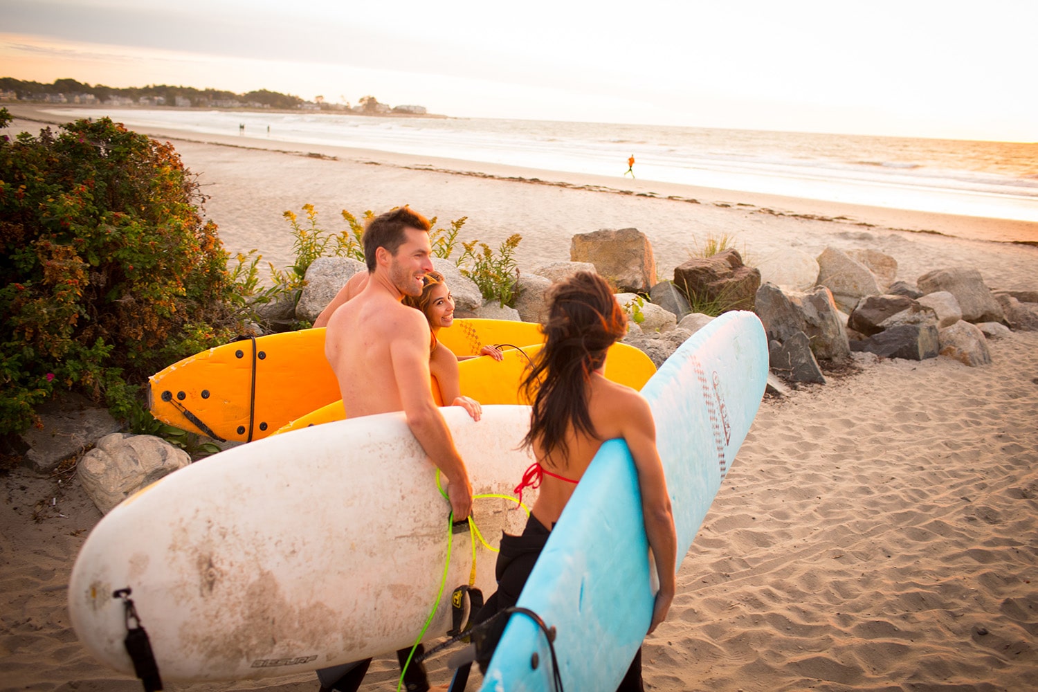 3 surfers walking towards the ocean with their surf boards smiling