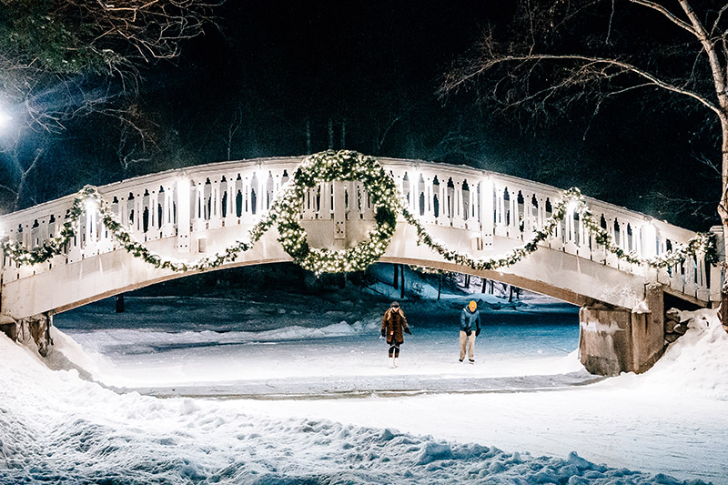 a couple skating under a lit up bridge